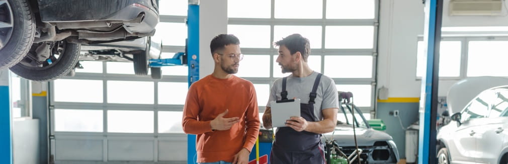 Rapaz jovem conversa com mecânico sobre a revisão do carro.
