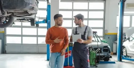 Rapaz jovem conversa com mecânico sobre a revisão do carro.