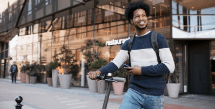 Jovem conhece legislação trotinete elétrica Portugal Jovem atravessa o passeio com uma trotinete elétrica na mão.