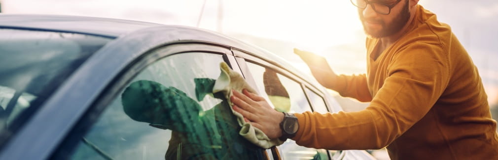 Rapaz a fazer limpeza automóvel ao exterior do seu carro.
