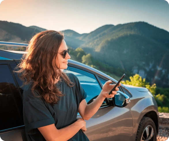 Jovem a olhar para o telemóvel a procurar o prestador local, encostada ao carro.