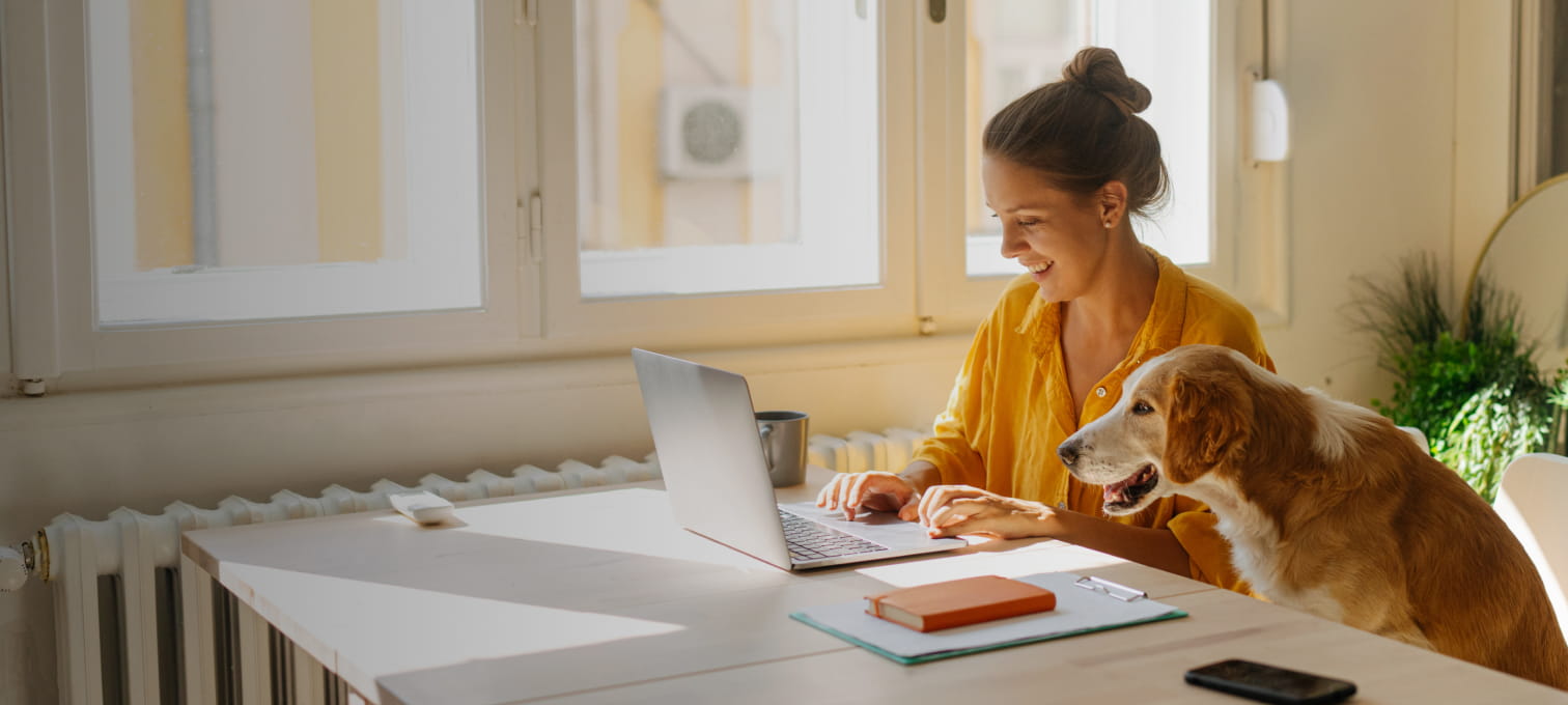 Mulher a trabalhar numa secretária, com um cão ao seu lado, num ambiente acolhedor.