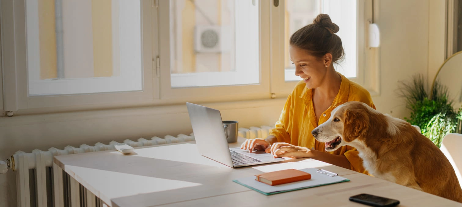 Mulher a trabalhar numa secretária, com um cão ao seu lado, num ambiente acolhedor.